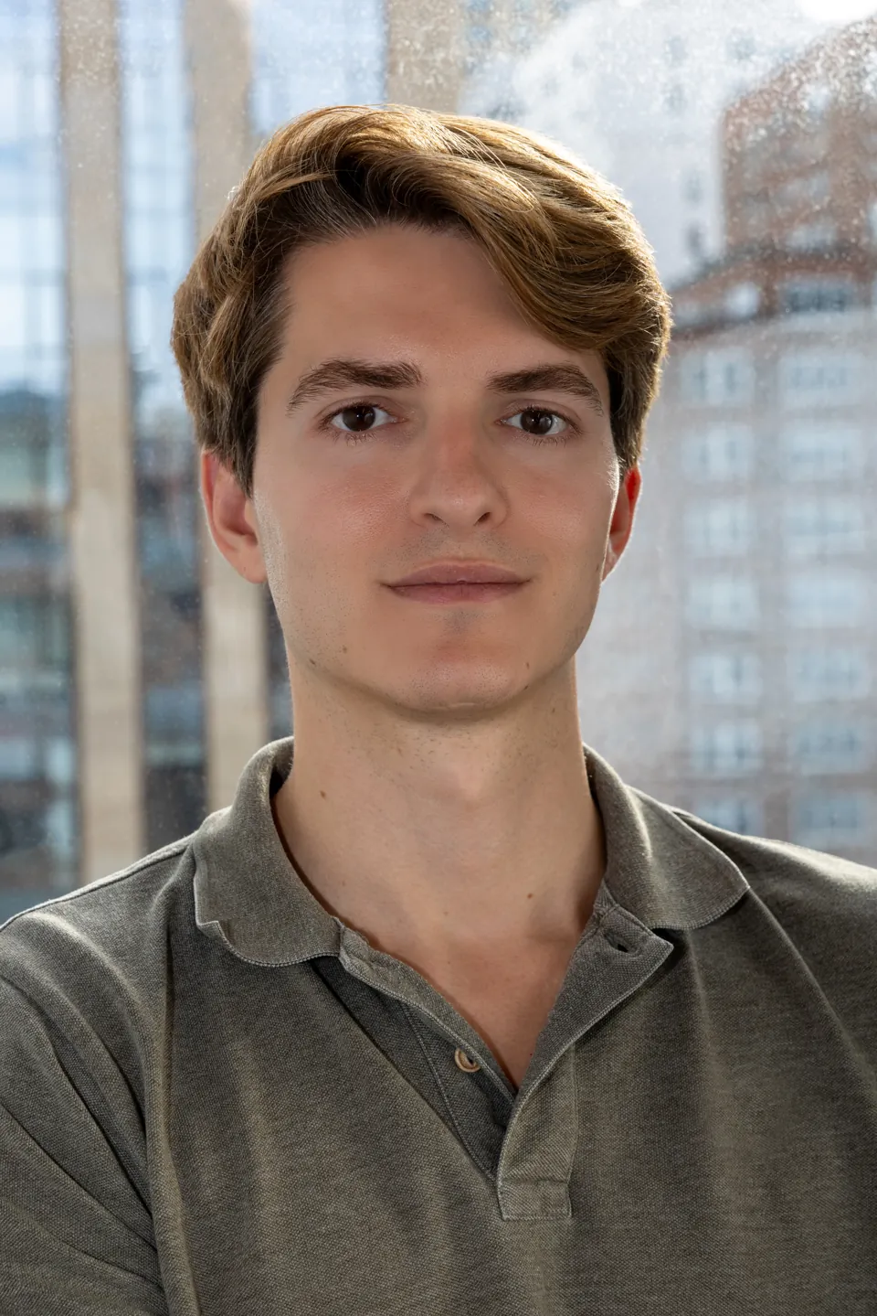 Portrait photograph of the artist Rafael de la Puente in front of a window overlooking New York buildings